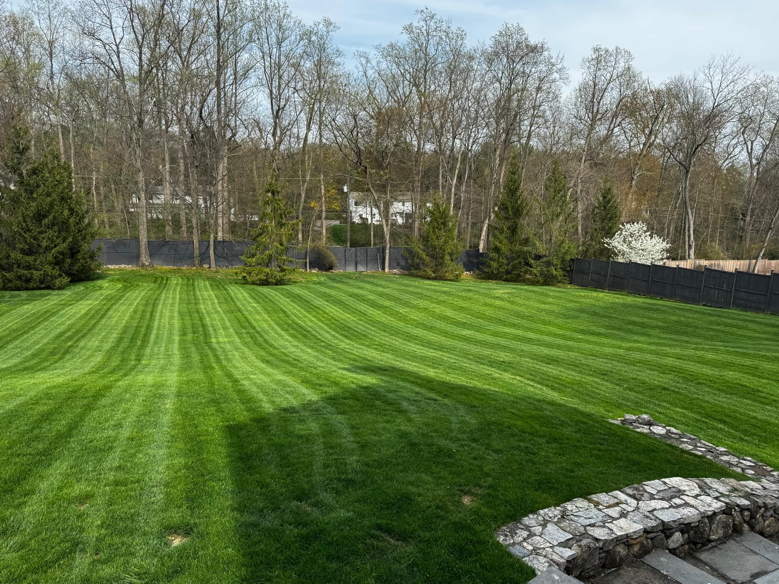 White colonial-style home with pristine lawn, white fence and stone wall